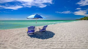 A beach with two striped beach chairs and a blue umbrella.
