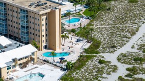 Un hôtel doté de plusieurs piscines, d’un espace de plage avec des chaises longues et d’un grand bâtiment à toit plat.