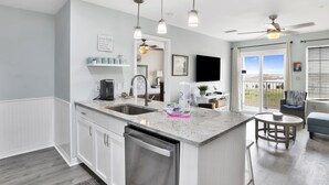 A modern kitchen with a central island, stainless steel appliances, pendant lighting, and a view to the outside. - 3BR @ Grand Beach Resort • Sleeps 8 • Balcony, Pool • Walk to Beach & The Hangout (Gulf Shores)