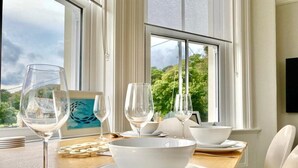 A dining table set with white plates, bowls, and wine glasses, with a view of greenery through large windows. - St Catherine's Lookout,  Niton, Isle of Wight (Niton)