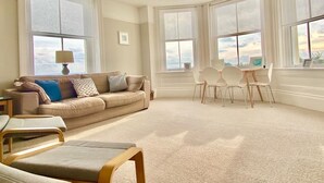 A spacious living room with a beige sofa, a dining table with chairs, and large windows offering a view of the sky and clouds. - St Catherine's Lookout,  Niton, Isle of Wight (Niton)