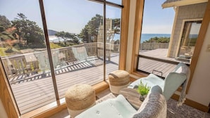 Een balkon met uitzicht op zee, een houten terras en een zithoek met een plant en kussens.