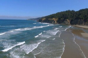 A coastal beach with waves, sandy shore, and forested cliffs. - Oceanfront Home Near Bandon Dunes Golf Discounted for Fall & Winter (Bandon)