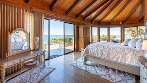 Een ruime slaapkamer met een groot bed, een kaptafel met spiegel, en uitzicht op zee door grote schuifdeuren.