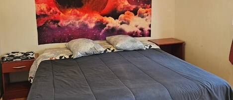 A bedroom with a large bed, a nightstand, a lamp, and a wall tapestry of a red moon.