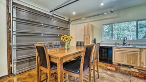 Una cocina con una mesa y sillas de madera, un ventanal con vista a árboles, y un puerta corrediza.