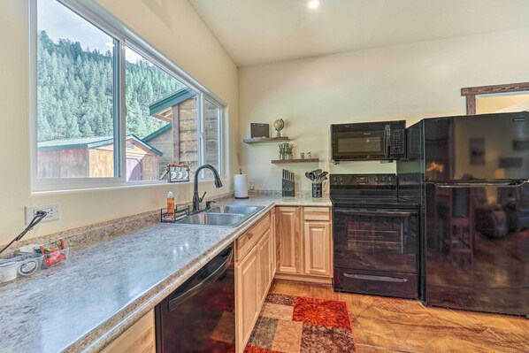 A kitchen with granite countertops, wooden cabinets, a black refrigerator, a microwave, and a dishwasher.