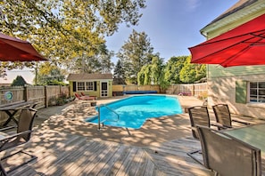 Eine Holzterrasse mit Pool, Gartenmöbeln und einem roten Sonnenschirm.