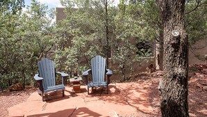 Two Adirondack chairs with a bottle and glasses on a stone patio surrounded by trees. - The Guest Dahl House of Sedona (Sedona)