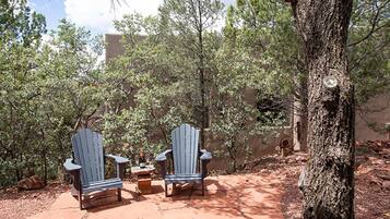 Deux fauteuils Adirondack, une bouteille et des verres sont posés sur une terrasse en pierre, le tout étant entouré d’arbres.