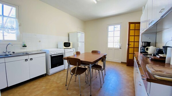 Una cocina compacta con gabinetes blancos, estufa, microondas y una mesa de comedor con sillas.