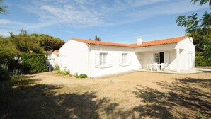 Edifici de color blanc amb teulada vermella, un porxo cobert amb cadires i un pati de terra.