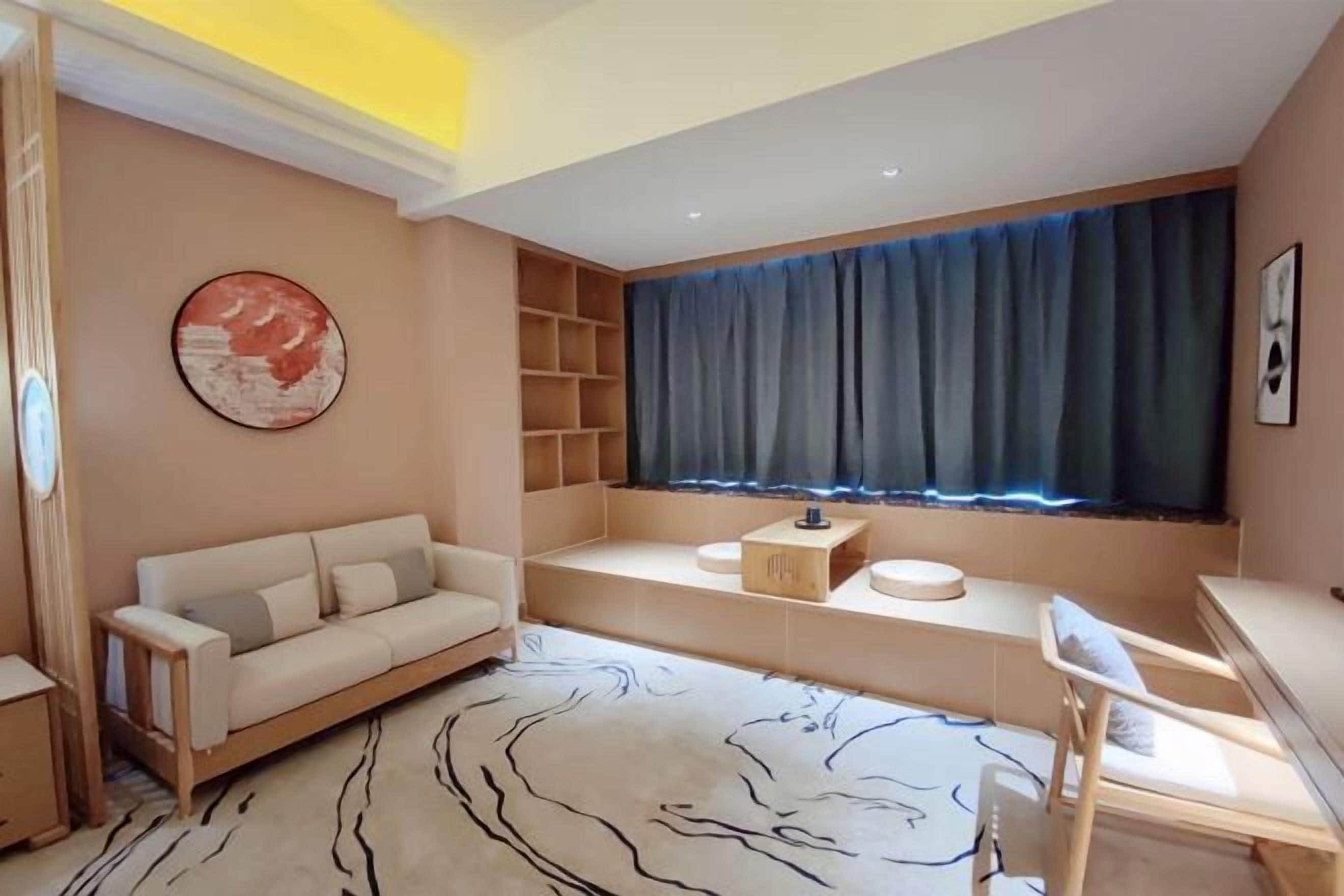 A modern living room with a sofa, a desk, a chair, a window with curtains, a round painting, and a patterned rug.