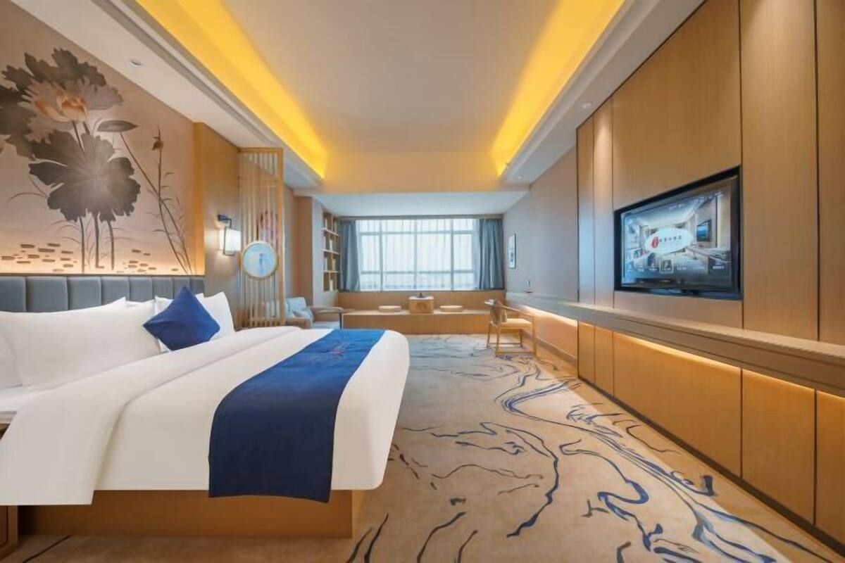 A modern hotel room with a large bed, a television, a seating area, and a view of the outdoors.