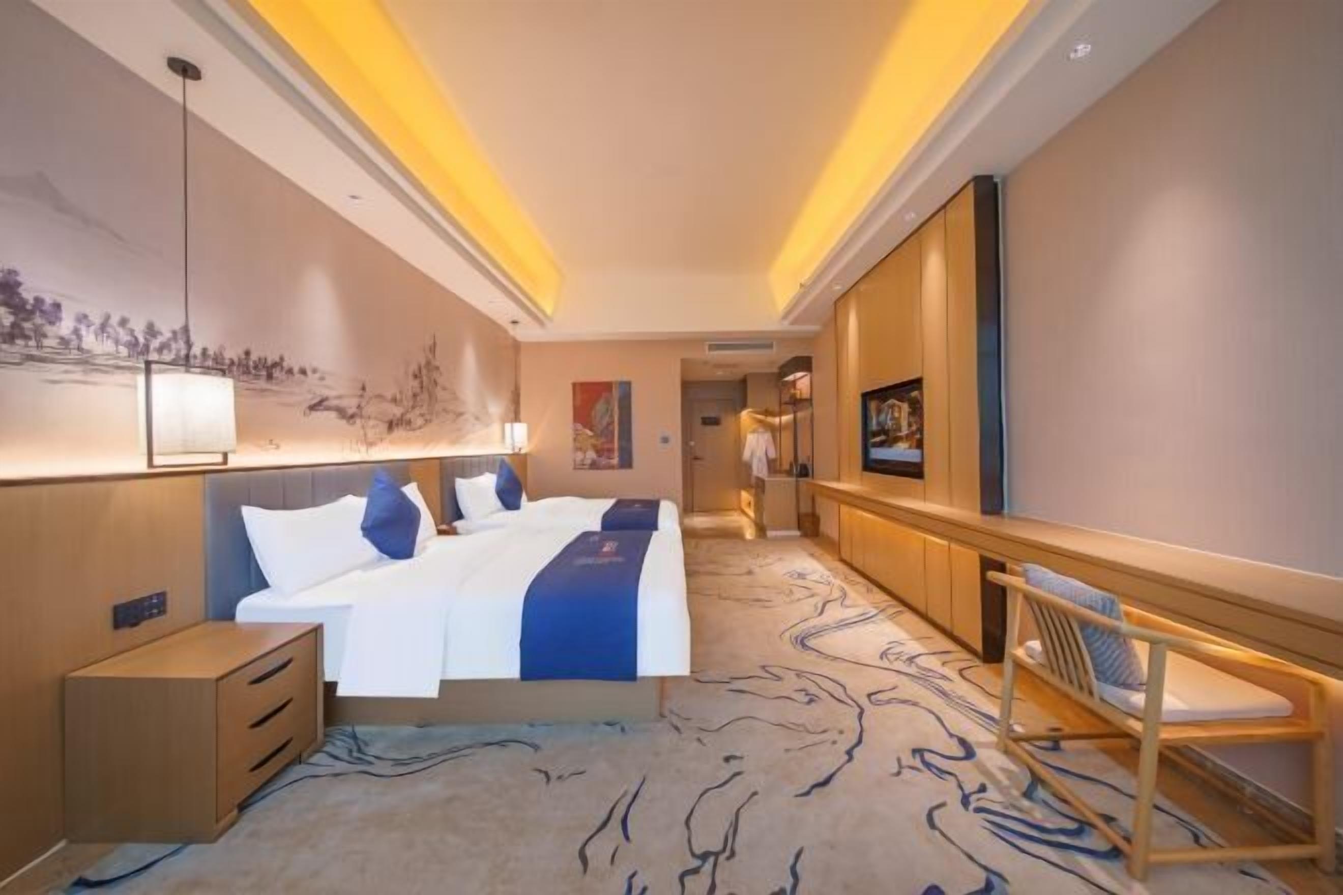 A hotel room with a large bed, a desk, a chair, and a TV.