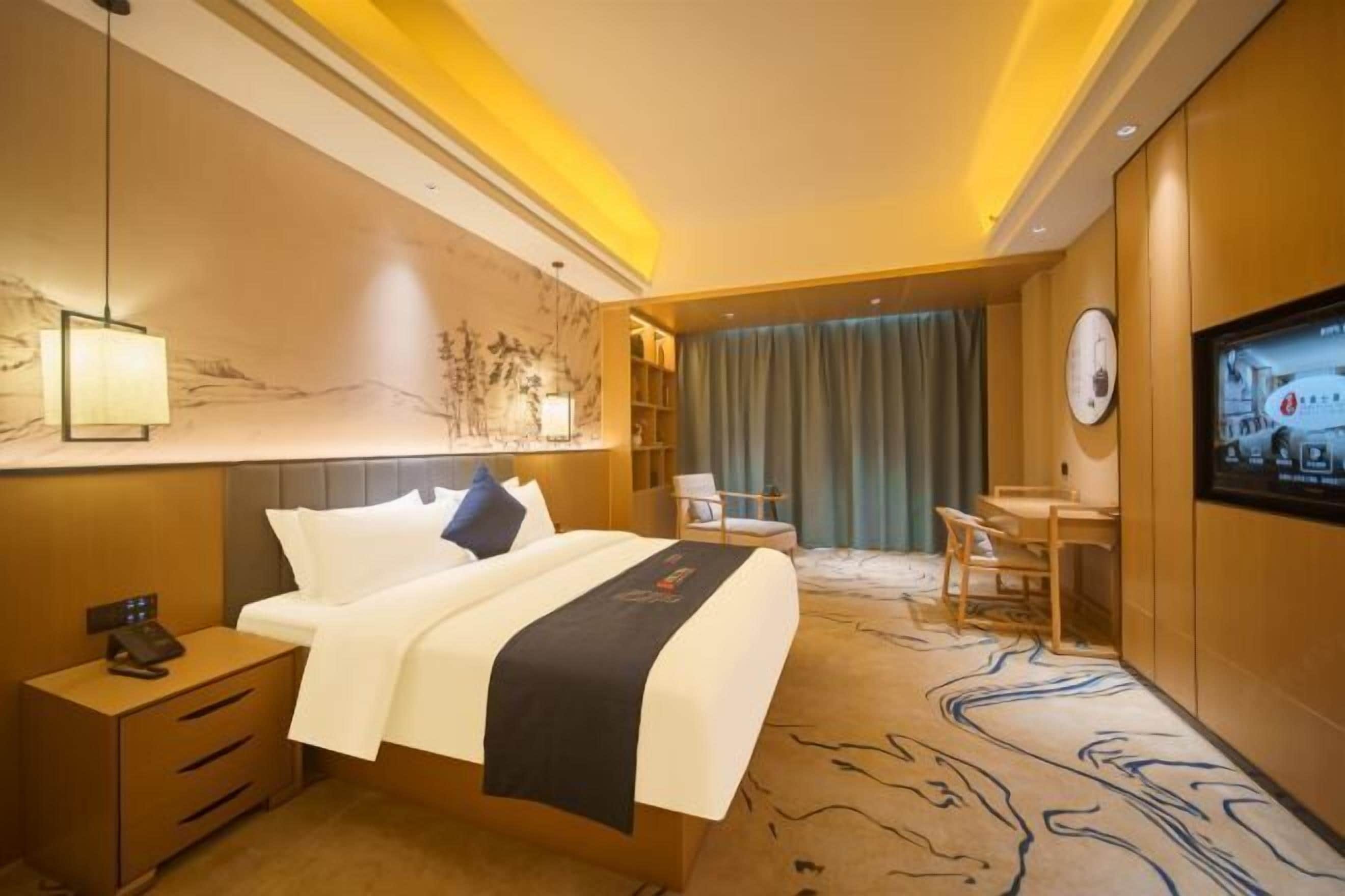A hotel room with a bed, bedside table, TV, and a desk with chairs.