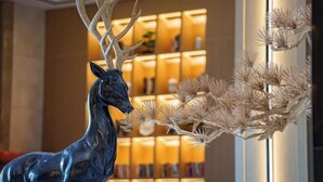 A sculpture of a deer with antlers in a lobby area with a warm, illuminated background and a decorative plant arrangement.