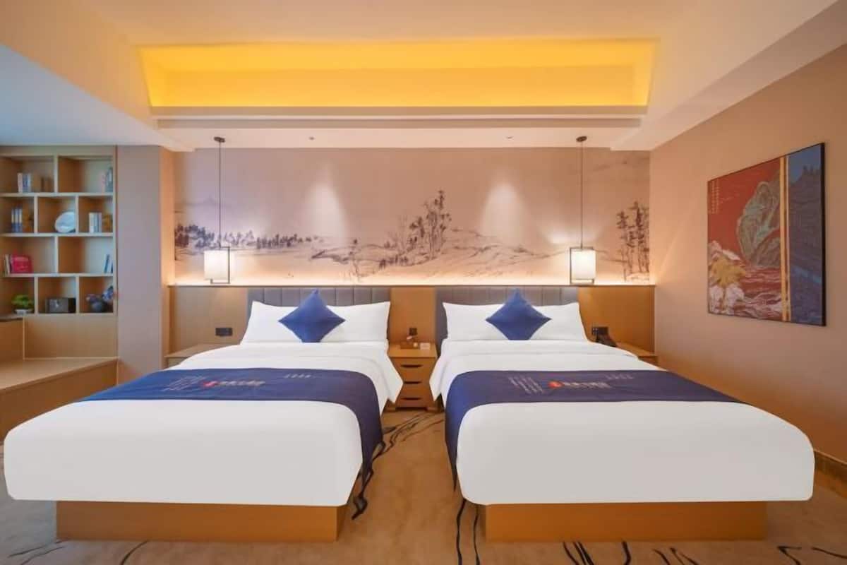 A hotel room with two beds, a bookshelf, a mural, and a painting on the wall.