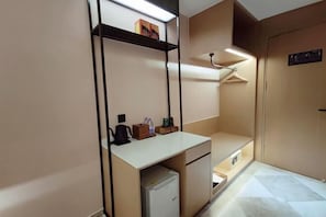 A compact hotel room with a kitchenette, a desk, and a wardrobe with hanging space.