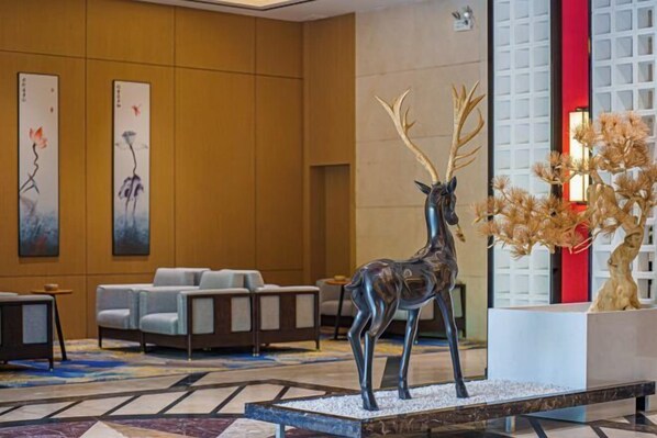 A lobby with a large deer sculpture, seating area, and artwork on the walls. - zhaona • Guofeng Intelligent Hotel (Dongguan)