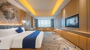 A hotel room with a large bed, a television, a seating area with a view of the city, and a decorative wall mural.