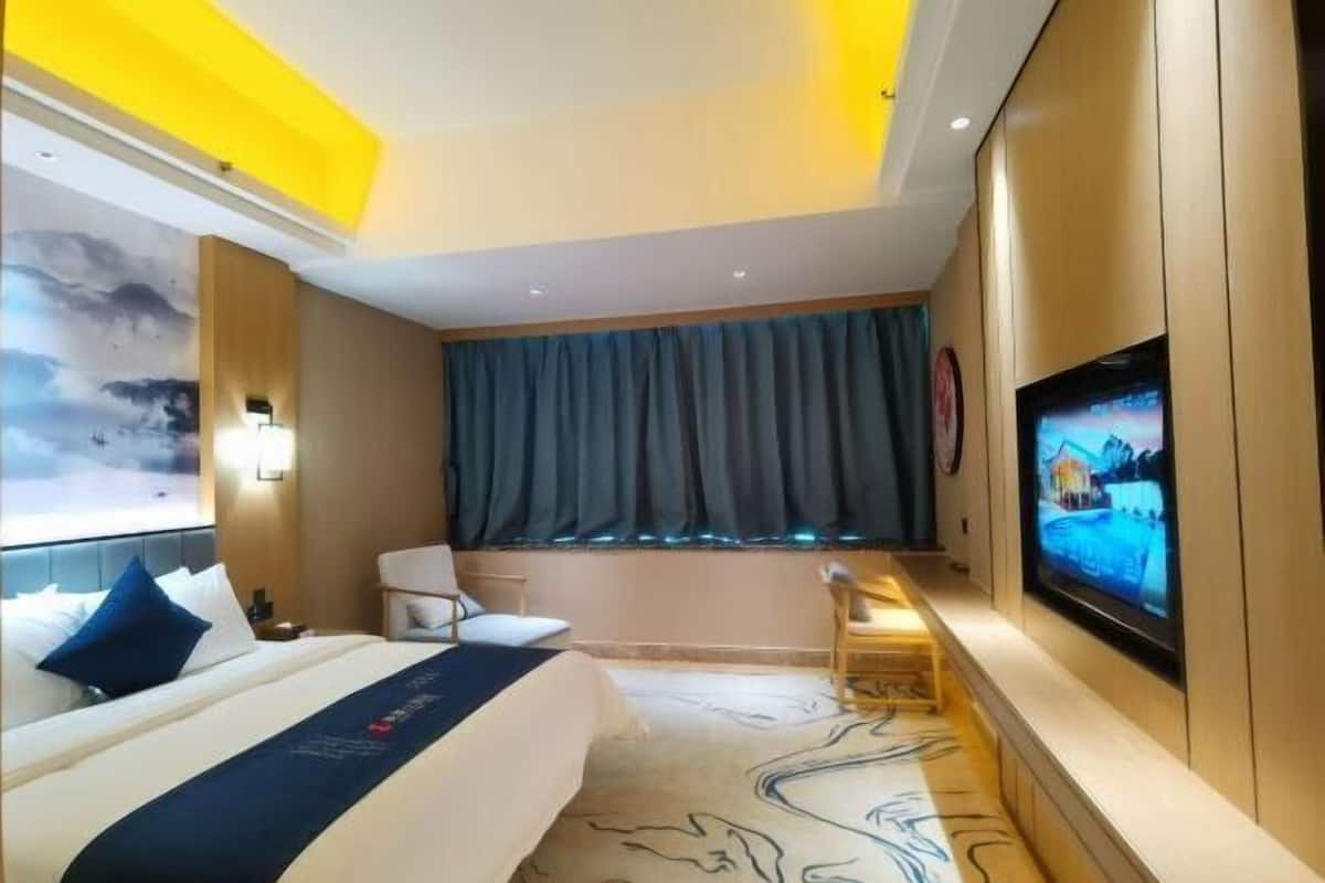 A hotel room with a bed, a desk, a chair, a TV, and a large window with curtains.
