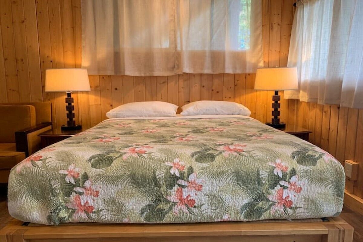 Una habitación con paneles de madera, una cama, dos lámparas de noche y una silla.