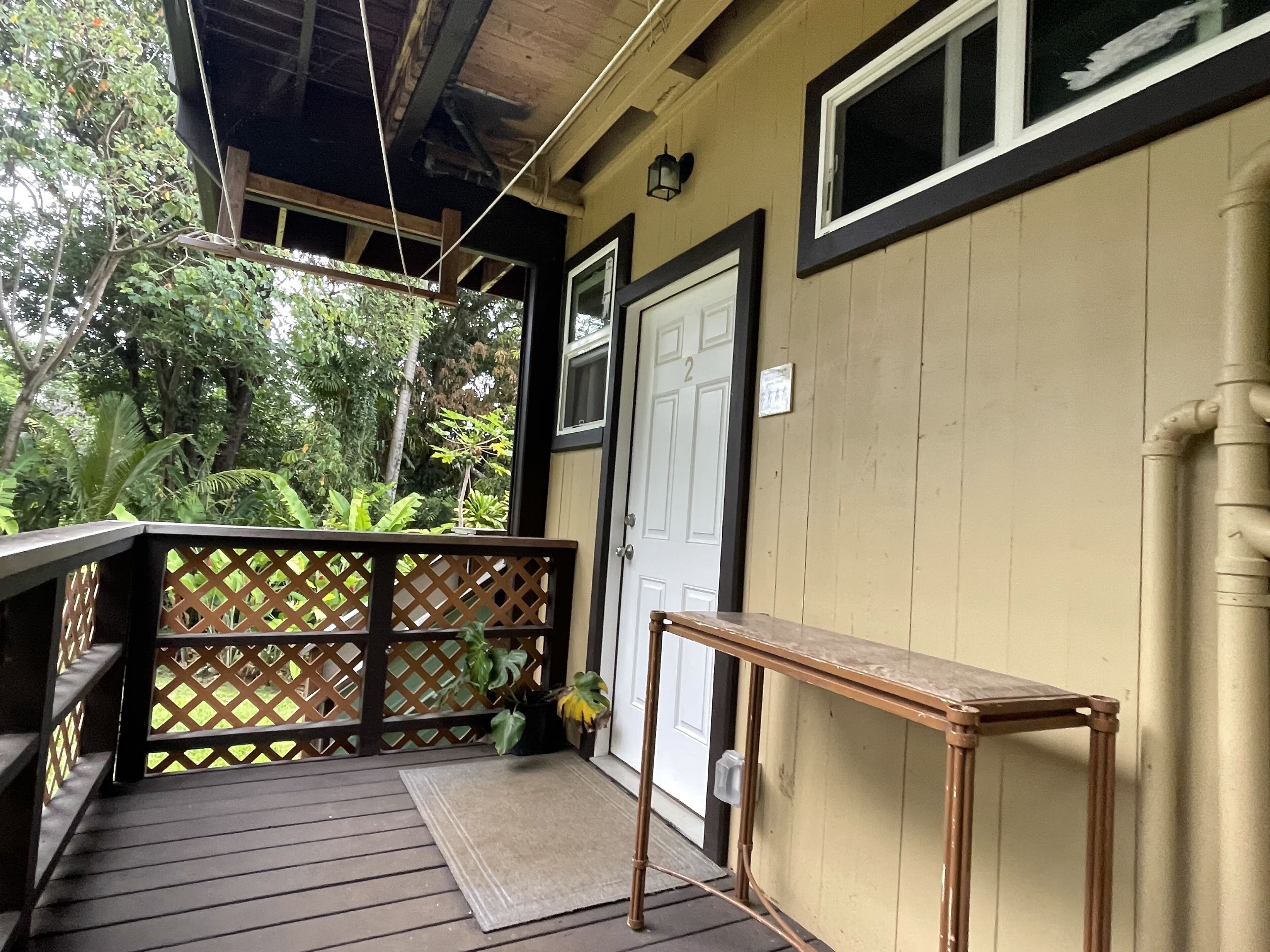A wooden porch with a bench, a door, and a view of greenery.