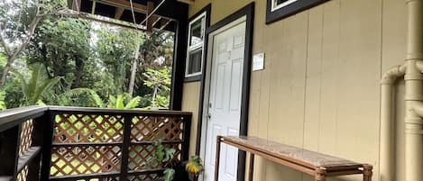 A wooden porch with a bench, a door, and a view of greenery.