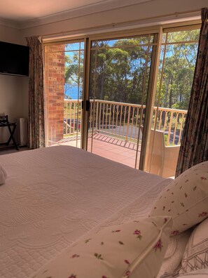 Een slaapkamer met een groot bed, uitzicht op een balkon met een hekwerk, en een bakstenen muur.