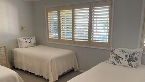 A bedroom with two single beds, a nightstand, a dresser, and a window with blinds. - 2 bedroom 2 bathroom apartment (Mollymook)