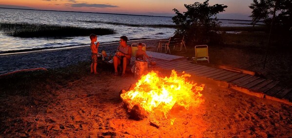 A beach scene with a fire pit, people sitting around it, and beach chairs. - Upper Red Lake all season destination! (Waskish)