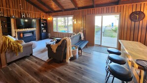 A cozy cabin interior with a fireplace, a sofa, a bar area, and a large window offering a view of the outdoors. - Upper Red Lake all season destination!  (Waskish)