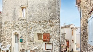 Une rue étroite bordée d’immeubles en pierre, avec un petit espace extérieur aménagé en terrasse et une boîte aux lettres bien visible.