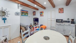 Un coin repas avec une table et des chaises blanches, un téléviseur et des œuvres d’art accrochées aux murs.