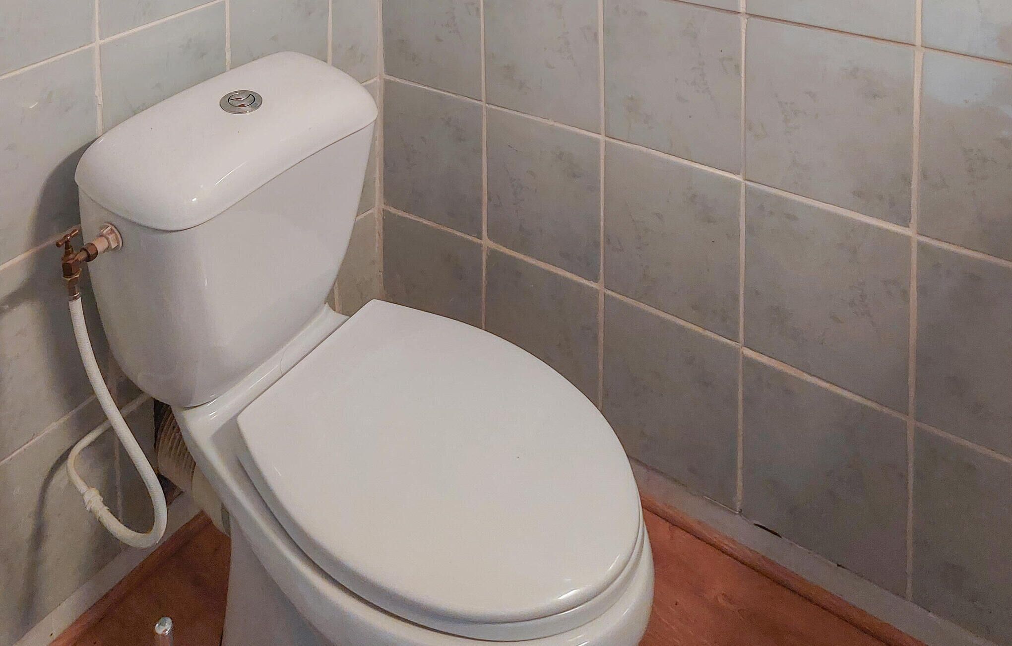 Eine weiße Toilette mit Tank und Spülhebel vor einer gefliesten Wand.