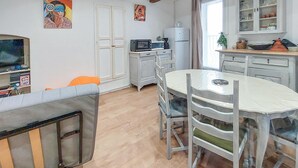 Un coin repas avec une table et des chaises blanches, un four à micro-ondes, un réfrigérateur et un meuble avec des portes en verre.