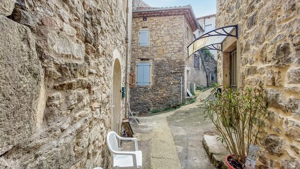 Une ruelle étroite bordée d’immeubles en pierre, une chaise en plastique blanche et un pot de fleurs.