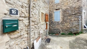 Une ruelle étroite pavée de pierres, avec une boîte aux lettres, une porte en bois et une fenêtre avec des volets.