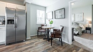 Una cocina moderna con un refrigerador de acero inoxidable, un comedor con dos sillas de cuero y una pequeña mesa redonda.