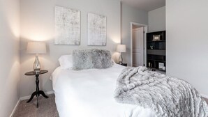 Un dormitorio ordenado con una cama, dos lámparas de noche, una mesita y una estantería.