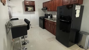 A compact kitchen with wooden cabinets, a black refrigerator, a microwave, and a gas stove. - Luxurious NYC Retreat / Central Location / Wi-Fi (Freeport)