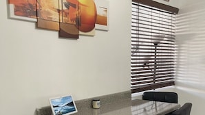A dining area with a glass-top table, four black chairs, a laptop on the table, and a window with blinds. - Luxurious NYC Retreat / Central Location / Wi-Fi (Freeport)