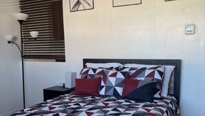 A bedroom with a geometric-patterned bedspread, a bedside table with a lamp, and three framed pictures on the wall. - Luxurious NYC Retreat / Central Location / Wi-Fi (Freeport)