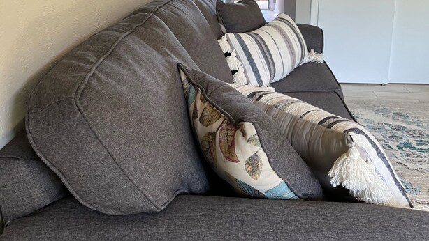 A gray sofa with multiple pillows, a wall clock, and a door in the background.