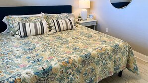 A neatly made bed with floral bedding, a bedside lamp, and a round mirror on the wall.