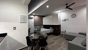 Un espace de vie moderne et compact comprenant un coin cuisine, un coin repas, un lit, un canapé et un ventilateur de plafond.