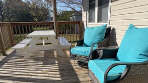 Une terrasse en bois avec une table de pique-nique et deux chaises en osier dotées de coussins turquoise.