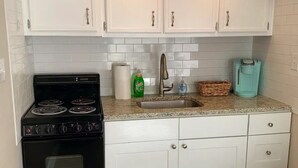 A kitchen with white cabinets, a black stove, a sink, and a teal coffee maker. - Capital City Condo #4 (Frankfort)
