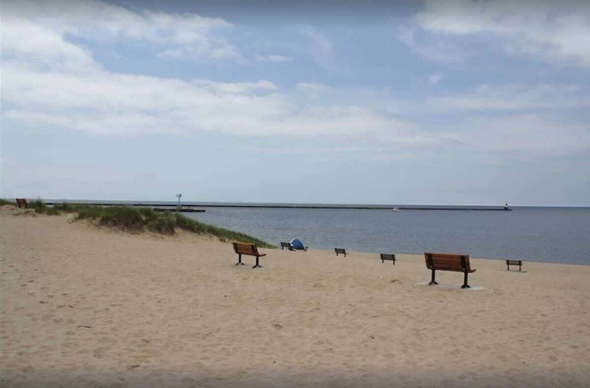 Une plage de sable avec plusieurs bancs en bois et une jetée qui s’avance dans l’eau.